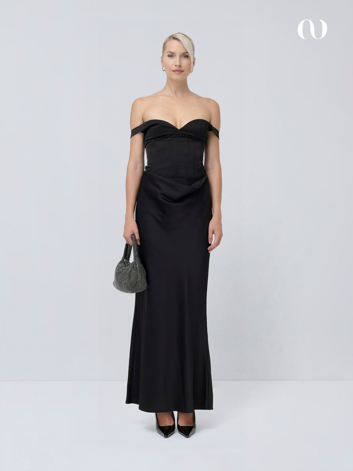 Eine Frau trägt ein schwarzes, schulterfreies „Jocelyn“-Kleid von LeGer by Lena Gercke mit Herzausschnitt und hält eine kleine, mit Metallperlen verzierte Handtasche in der Hand.