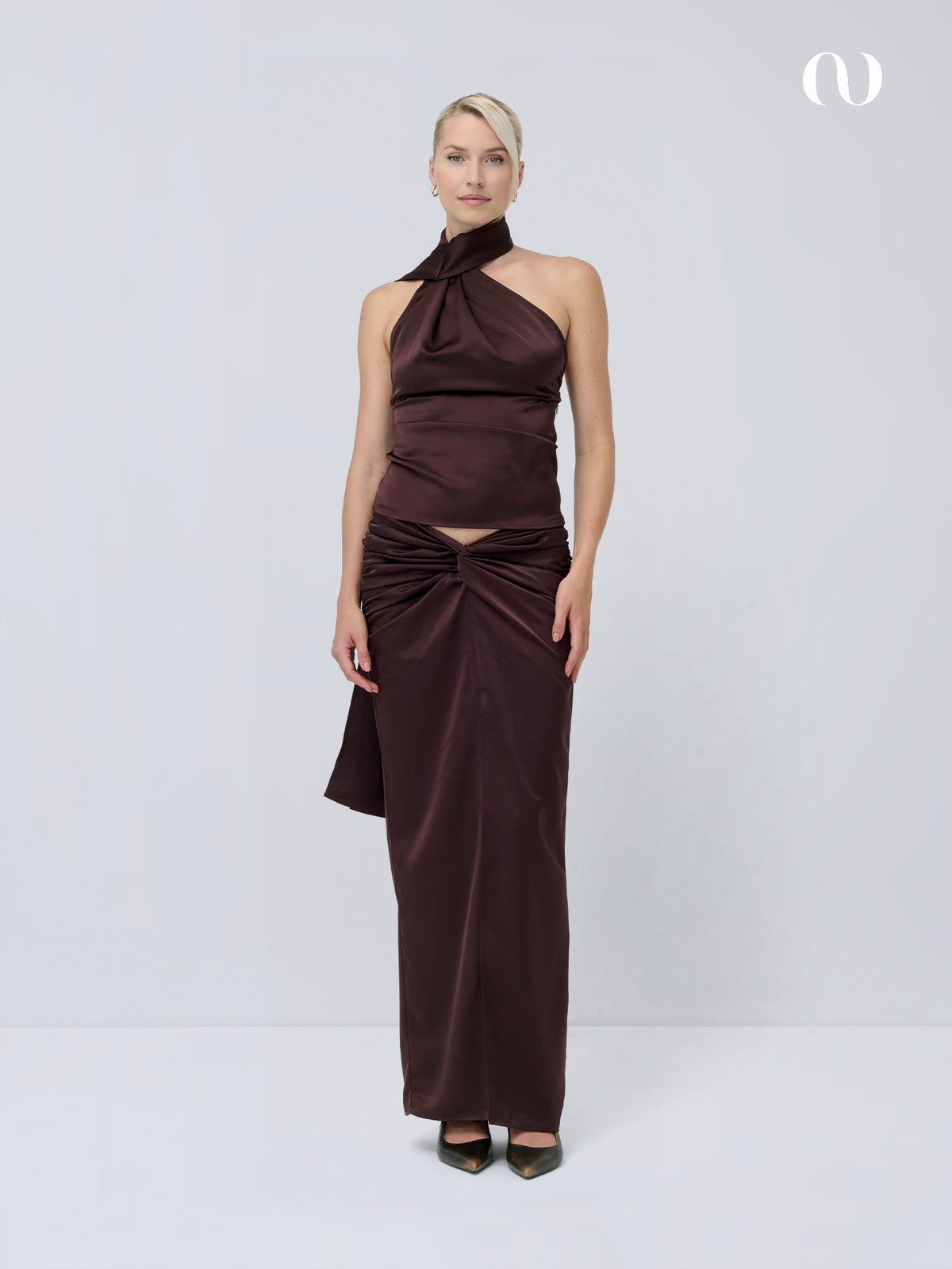 Ein Model trägt ein dunkelbraunes Neckholder-Oberteil und den dazu passenden Rock „Josephin“, dessen geknotetes Taillendetail eine lange Silhouette zaubert.