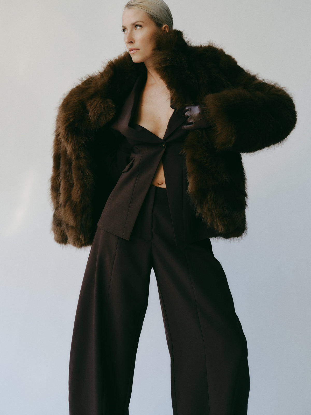 Das Model trägt eine dunkelbraune „Dion“-Jacke in luxuriöser Felloptik über einem passenden Blazer und einer Hose mit weitem Bein.
