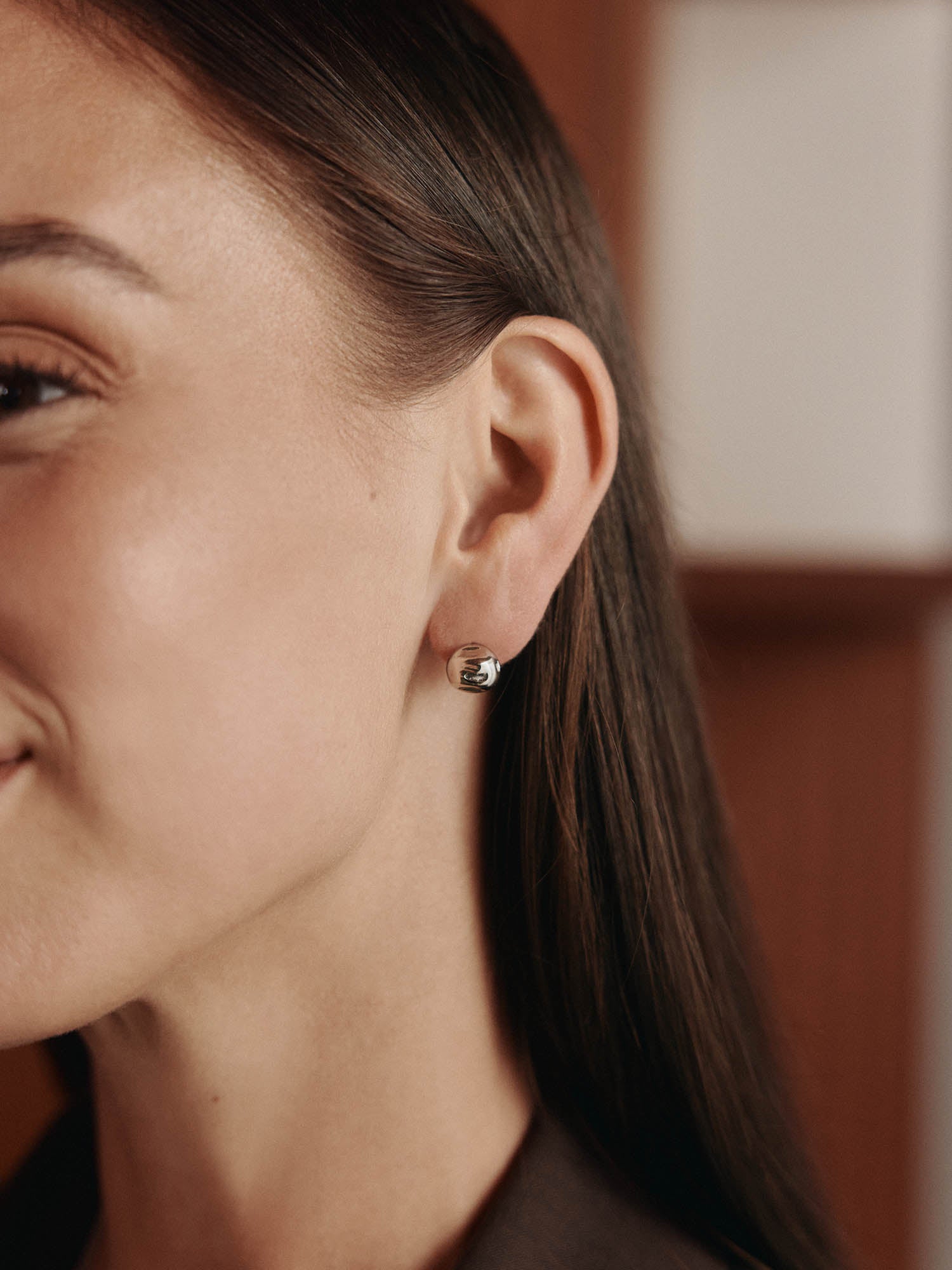 Eine Nahaufnahme zeigt das Ohr einer Frau, das mit kleinen, silbern glänzenden Ohrringen von LeGer x Purelei - Unstoppable Ohrringe by LeGer by Lena Gercke - geschmückt ist. Ihr glattes braunes Haar ist zurückgesteckt, und ein Weichzeichner-Hintergrund verstärkt die elegante Ausstrahlung.